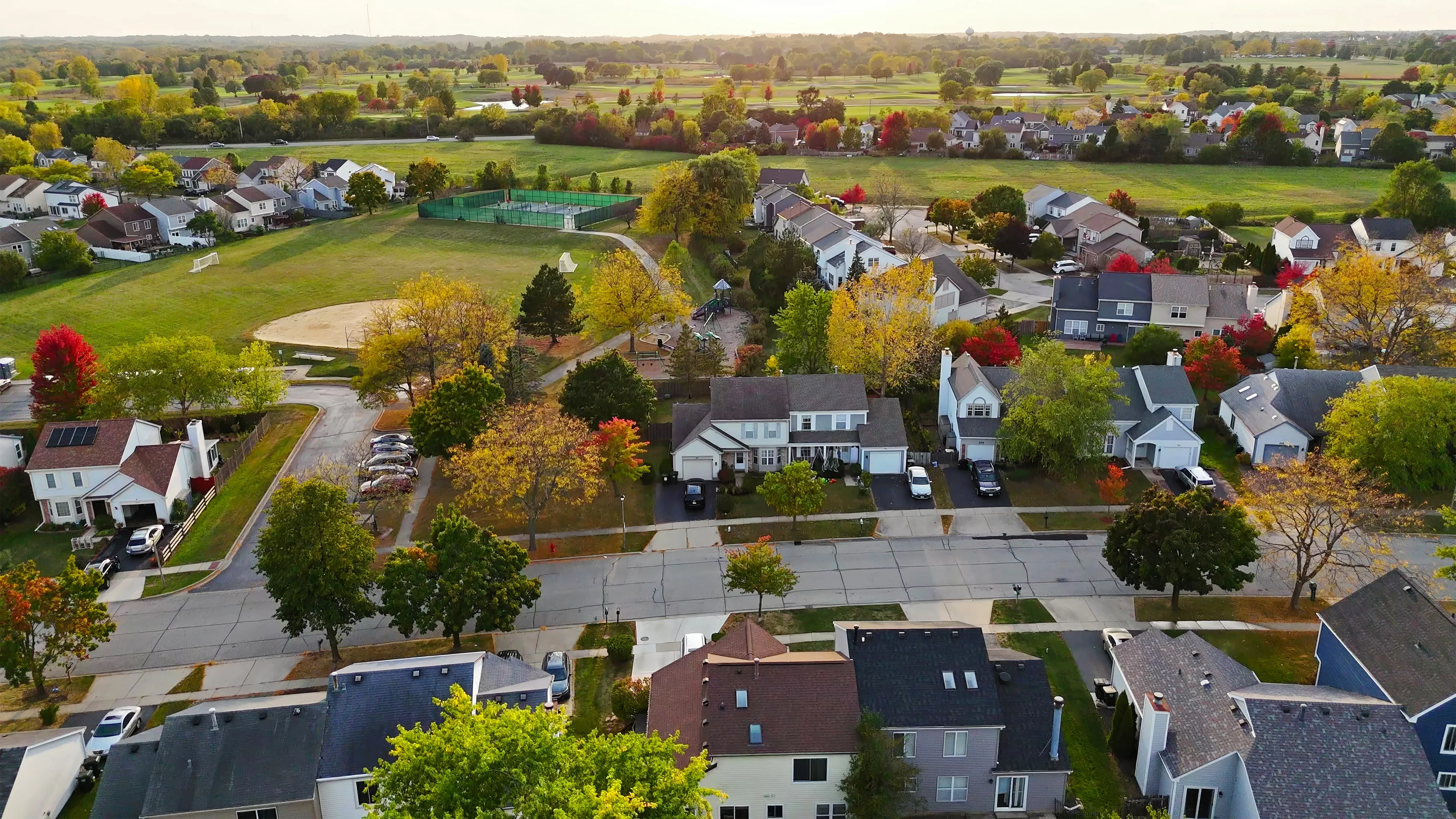 An aerial view of an established suburban neighborhood in autumn, its streets and parkland backing onto a golf course.